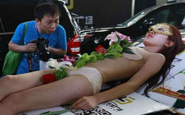 Một người đàn ông không giấu nổi vẻ mặt thích thú khi nhìn cô nàng bán khỏa thân nằm trên nắp capô Nissan GT-R để phục vụ món sushi.