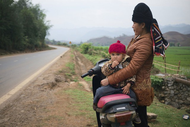 Một phụ nữ Việt đặt con nhỏ trên yên xe máy.