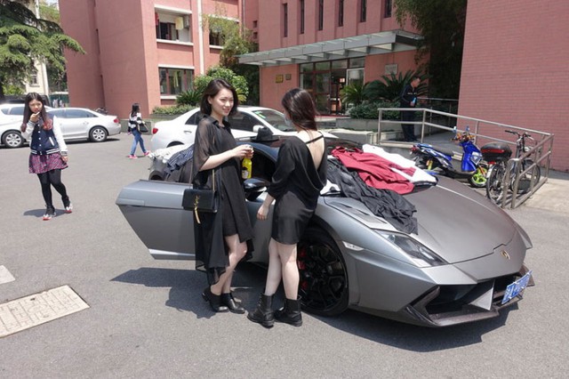 Hai cô nàng xinh đẹp đứng cạnh chiếc siêu xe Lamborghini được phủ đầy quần áo lên trên.