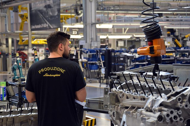 Một công nhân mặc đồng phục màu đen có dòng chữ “Produzione” màu vàng sau lưng. Trong tiếng Ý, “produzione” có nghĩa là “sản xuất”. Như vậy, đây là một công nhân làm việc tại xưởng lắp ráp.