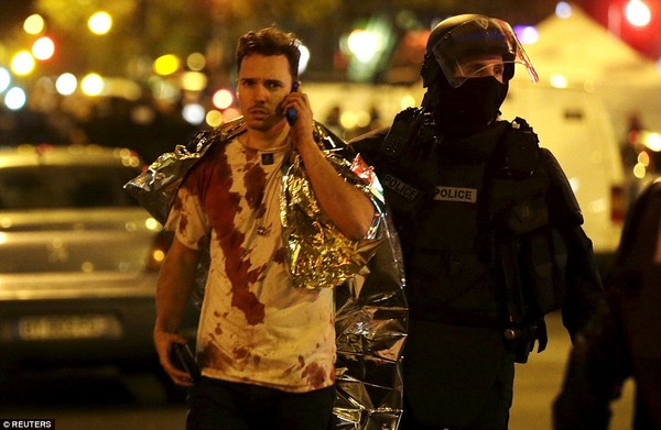 Cảnh sát đưa một nạn nhân với chiếc áo đẫm máu ra khỏi khu vực phong tỏa nhà hát Bactalan. Tổng thống Hollande đã ban bố tình trạng khẩn cấp và gọi đây là vụ khủng bố chưa có tiền lệ. Ông cũng đã yêu cầu đóng cửa biên giới.  Ảnh: Reuters.