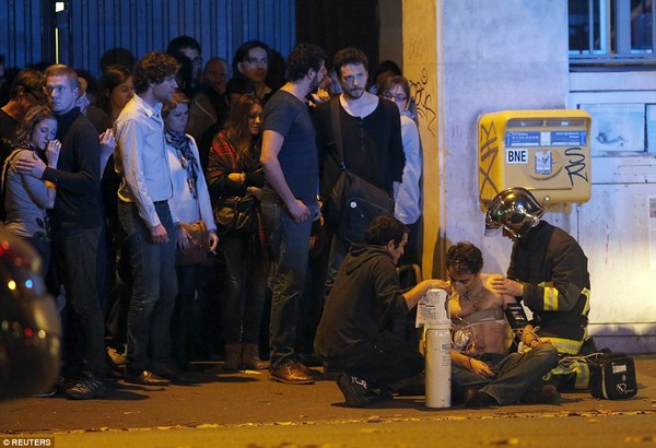 Nhân viên cứu hộ đang băng bó cho nạn nhân bị thương bên ngoài rạp chiếu phim Bataclan trong khi những người khác vẫn hoảng loạn sau sự việc. Theo nhà chức trách Pháp, lực lượng an ninh đã tiêu diệt hai phần tử khủng bố tại rạp chiếu phim. Ảnh: New York Times
