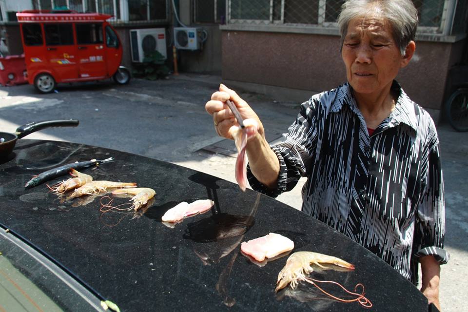 
Người phụ nữ lớn tuổi nướng tôm và thịt trên cốp xe hơi.
