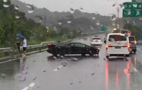 
Cặp đôi nam nữ đứng che ô bên cạnh chiếc Lamborghini Aventador bị tai nạn.
