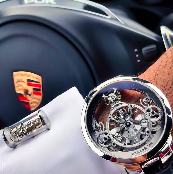 Vẻ đẹp ấn tượng của chiếc đồng hồ Arnold & Son Time Pyramid bên cạnh vô lăng của chiếc xe thể thao Porsche. Với thiết kế skeleton (lộ cơ) độc đáo và kiến trúc tam giác là lý do chiếc đồng hồ này được đăt tên “Pyramid”.