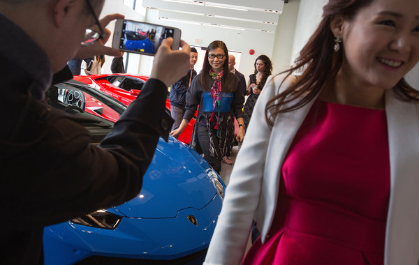 
Một người đàn ông chụp ảnh vợ bên chiếc siêu xe Lamborghini mới tại đại lý.
