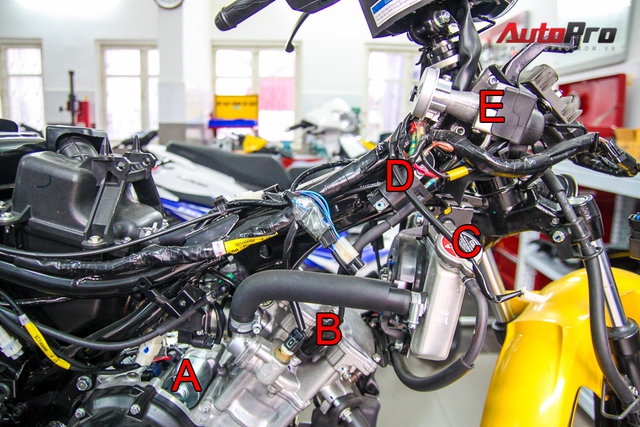 
Các chi tiết máy nhìn từ hông xe: A: củ đề, B: Bugi (đen), C: miệng két nước, D: mô-bin, E: ổ khóa.
