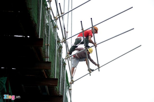 Phía trên, công nhân mặc thường phục thắt dây bảo hiểm đứng chênh vênh làm việc.