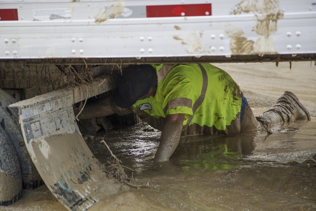 
Một số công nhân còn phải đào bùn đất bằng tay để giải cứu những chiếc ô tô bị mắc kẹt. Trong ảnh là một công nhân đang bò dưới thùng sau của xe đầu kéo để dọn hỗn hợp giữa bùn đất và rác rưởi.
