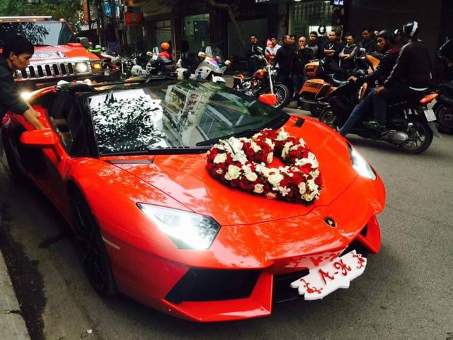 
Aventador nổi bật trên phố trong bộ áo đỏ bắt mắt, ngoài ra hoa cưới hình trái tim được trang trí đơn giản trên nắp capô xe. Cản trước được trang trí ấn tượng với tên viết tắt của chú rễ và cô dâu.
