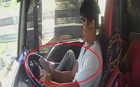 Tài xế dùng chân điều khiển xe đầu kéo chạy trên cao tốc, tay cầm điện thoại lướt TikTok